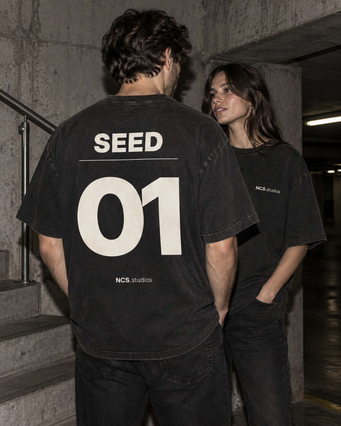 Zwei Menschen in Washed Black NCS.studios Shirts im Beton-Treppenhaus, Seed 01 als Rückenprint